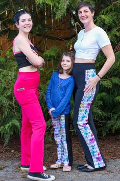 three women standing next to each other in front of trees