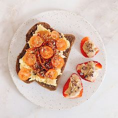 a white plate topped with toast covered in toppings next to sliced oranges and an avocado