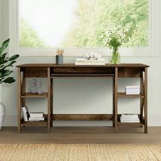 a wooden desk sitting in front of a window next to a vase with flowers on it