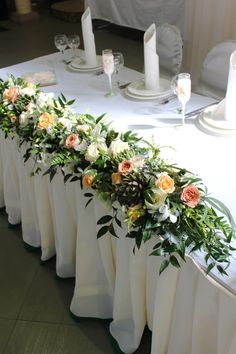 the table is set with white linens and flowers on each side, along with candles