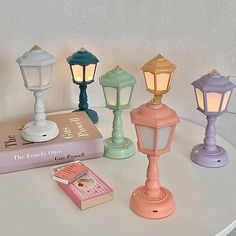 four different colored lamps sitting on top of a table next to a book and lamp