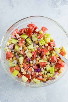 a glass bowl filled with chopped vegetables on top of a white countertop next to a metal spoon