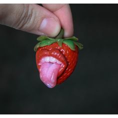 a hand holding a fake strawberry with its tongue out and it's tongue sticking out