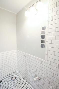 a bathroom with white tile and black grouting on the walls, along with a shower head