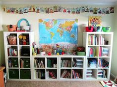 a room filled with lots of books on top of white shelving unit units next to a wall mounted map