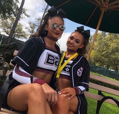 two cheerleaders are sitting on a bench under an umbrella and posing for the camera