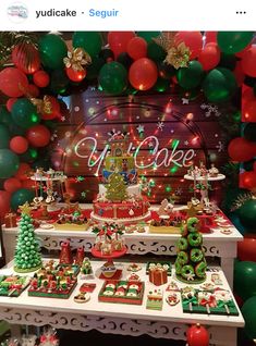 a christmas themed dessert table with balloons and garlands on the wall, decorated in red green and gold