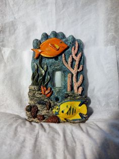 an orange fish sitting on top of a rock next to some corals and seaweed