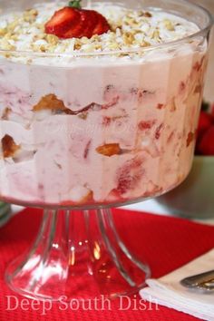 a dessert with strawberries and cream in a glass dish on a red tablecloth