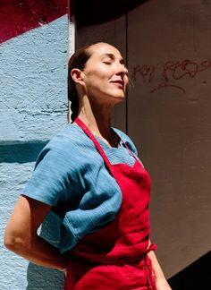 a woman wearing an apron standing in front of a blue wall with graffiti on it