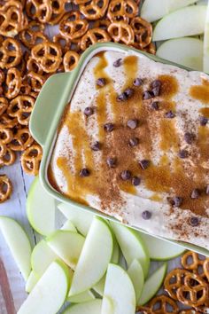 an ice cream dish with chocolate chips on top surrounded by apples and pretzels