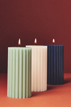 three candles sitting next to each other on top of a red surface with one candle lit