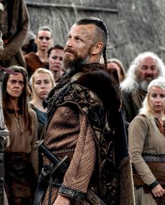 a man with dreadlocks standing in front of a group of people wearing medieval clothing