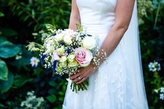 a bride holding a bouquet of white and pink flowers on her wedding day in front of greenery