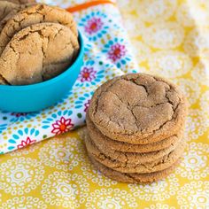 a blue bowl filled with cookies on top of a yellow and white table cloth next to a stack of cookies