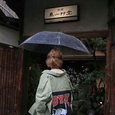 a woman holding an umbrella standing in front of a building with chinese writing on it