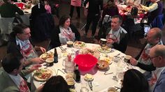 a group of people sitting around a white table eating food and drinking wine at an event