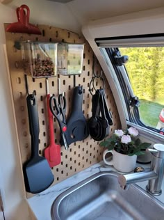 a kitchen sink with utensils hanging on the wall next to it and a window