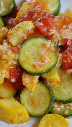 a white plate topped with zucchini and tomato sauce next to sliced cucumbers