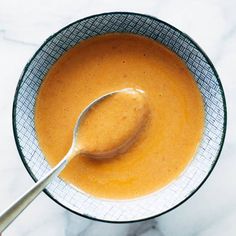 a spoon is in a bowl filled with orange liquid on a marble counter top,