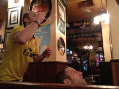 a man in a yellow shirt drinking from a wine glass while another man looks on