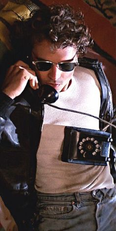 a man in sunglasses talking on a phone while holding an old fashioned telephone to his ear