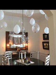 a dining room table with white chairs and balloons hanging from it's ceiling in front of a mirror