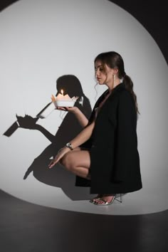 a woman holding a cake with a candle on it in front of a white wall