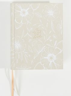 a small notebook with white flowers on the front and back cover, sitting against a white background