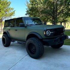 a large green truck parked on top of a cement driveway next to trees and grass