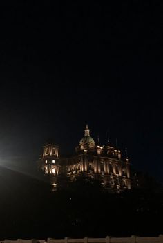 a large building lit up at night with the moon in the sky and light shining on it