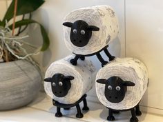 three sheep made out of toilet paper sitting on top of a counter next to a potted plant