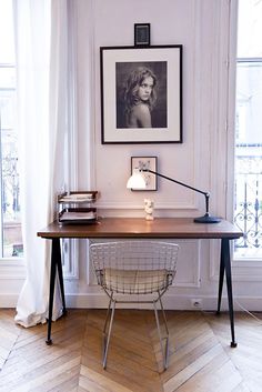 a desk with a lamp and pictures on the wall above it in front of a window