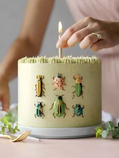 a woman lighting a candle on top of a cake with bugs on the frosting