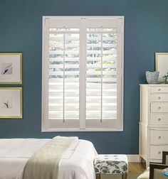 a bedroom with blue walls, white furniture and shutters on the window sill