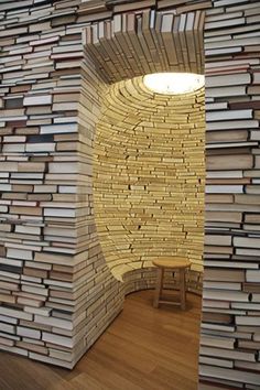 a room made out of books with a lamp on the wall and a stool in front of it