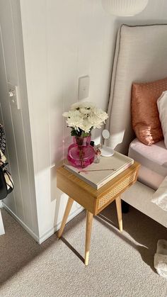 a small table with flowers on it next to a white chair and bed in the background