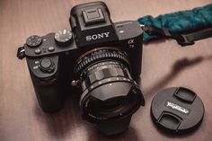 a sony camera sitting on top of a wooden table next to a lens cap and an adapter