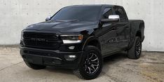 a black truck is parked in front of a white wall and cement floored area