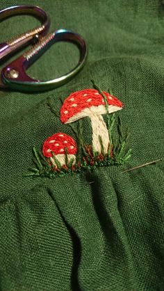 a pair of scissors sitting on top of a piece of green cloth next to mushrooms