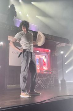 a man standing on top of a stage with his hands in his pockets while holding a microphone