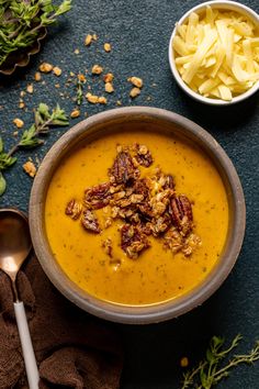 a bowl of soup with nuts and cheese on the side, next to a spoon