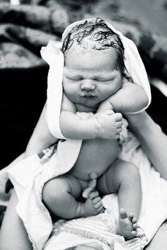 a black and white photo of a baby wrapped in a towel with its head on his mother's shoulders