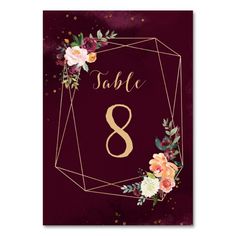 a table number card with flowers and gold foil on maroon paper, in the shape of an octagon