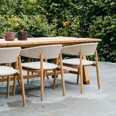 a wooden table with four chairs sitting on top of it next to a green bush