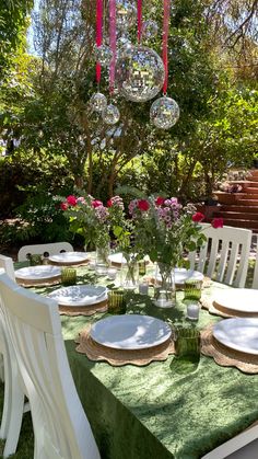 the table is set with plates and flowers in vases on it, near some trees