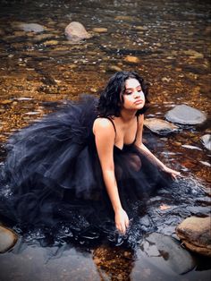 a woman is sitting in the water wearing a black dress