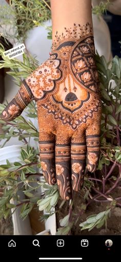 a hand with henna on it and some plants in the back ground next to it