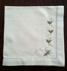 a white cloth with daisies and green leaves embroidered on the side, sitting on a wooden surface