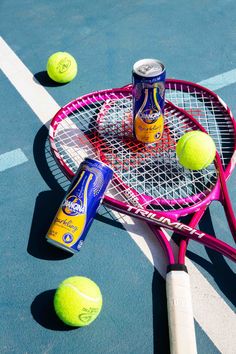 two tennis rackets and three cans of beer are on the court next to balls